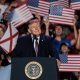 Donald Trump speaking at a rally with supporters holding American flags in the background, highligh — Trump mail-in voting