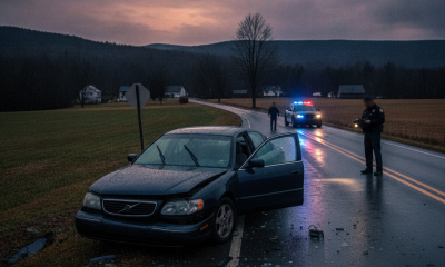 Vermont State Police Shaftsbury Barracks officers investigate a damaged sedan on a wet rural road at dusk.