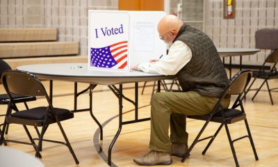 A voter sitting at a table in a polling place, marking a ballot behind a privacy screen w — election betting laws by state
