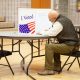 A voter sitting at a table in a polling place, marking a ballot behind a privacy screen w — election betting laws by state