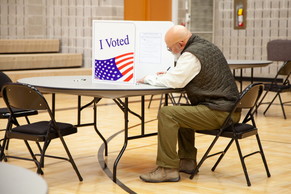 A voter sitting at a table in a polling place, marking a ballot behind a privacy screen w — election betting laws by state